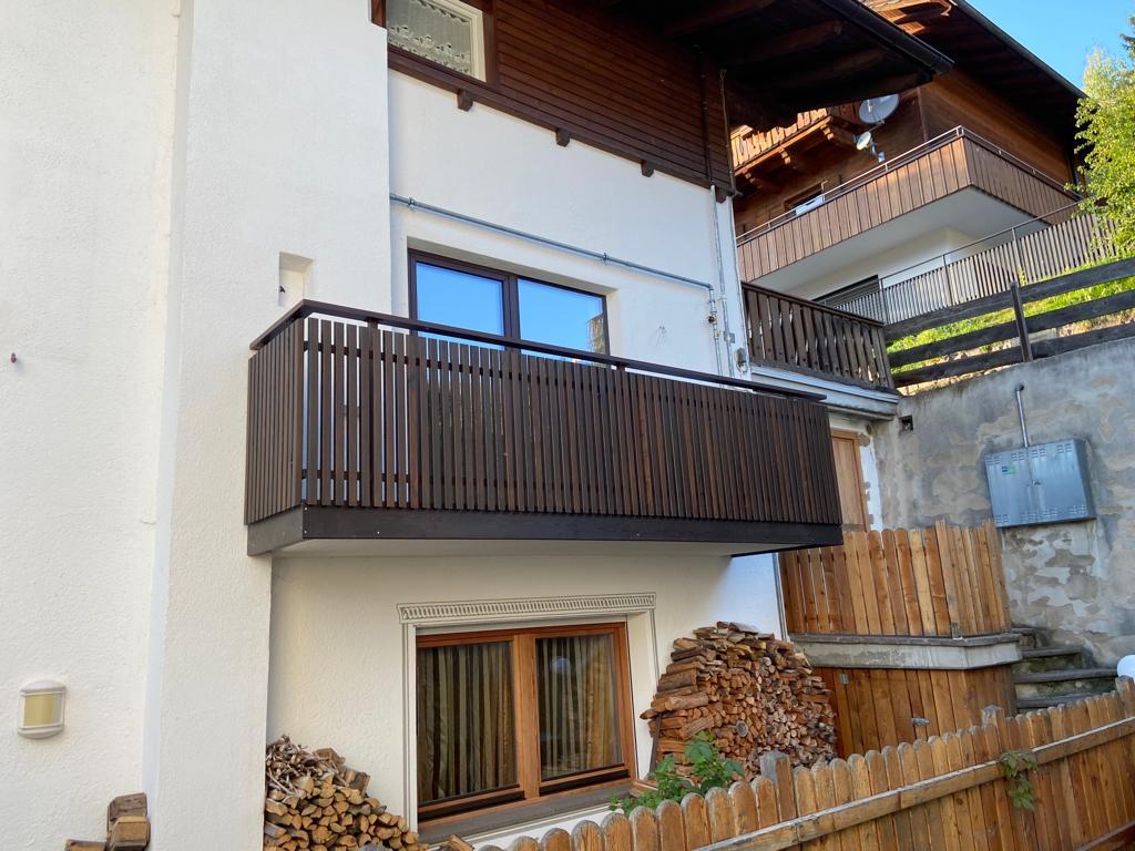 Stäbchenbalkon aus dunkel gestrichener Lärche mit Sockel und Lärchenholz-Handlauf
